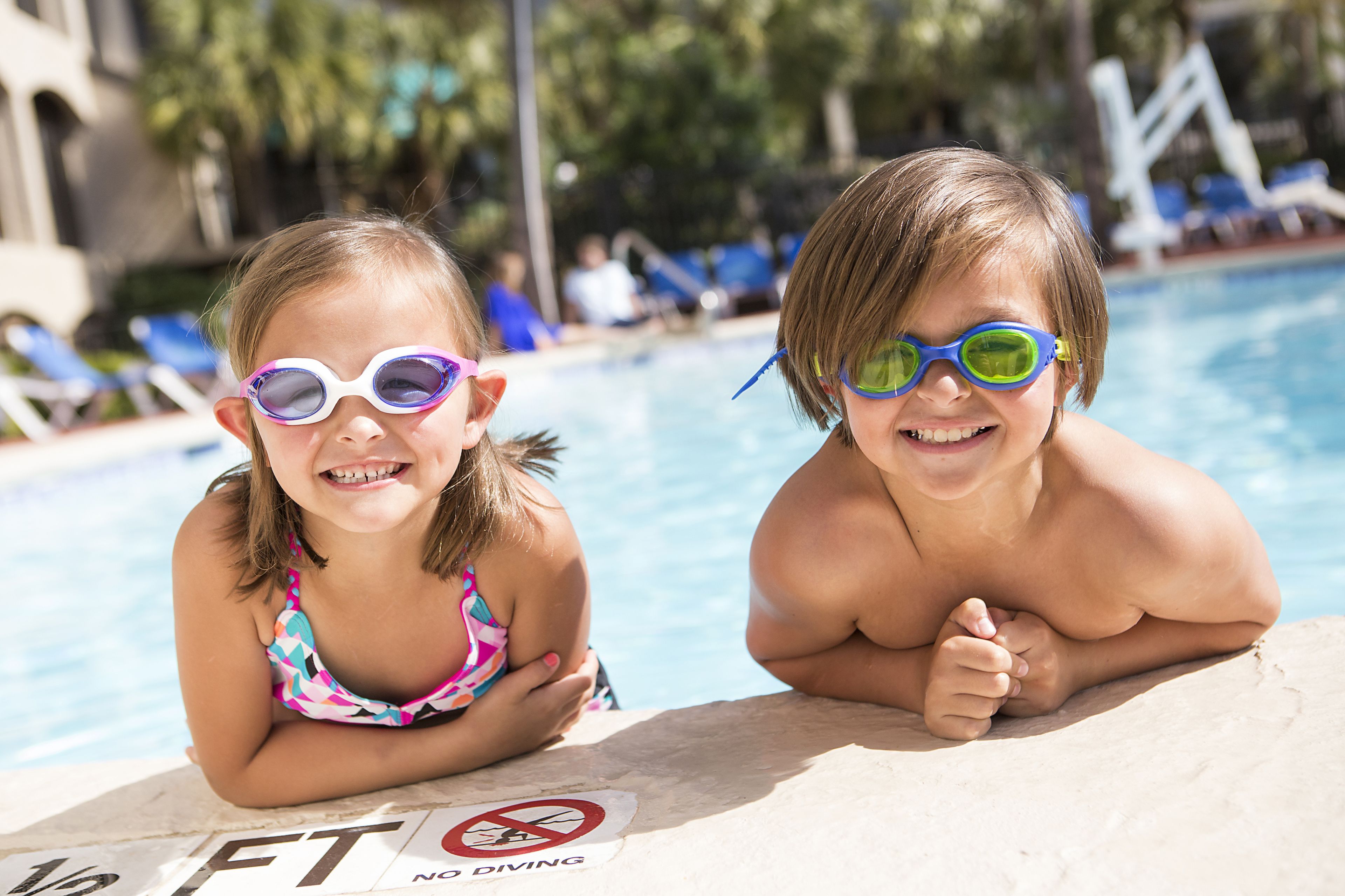 Deux enfants près d’une piscine, avec un panneau indiquant « Il est interdit de plonger ».