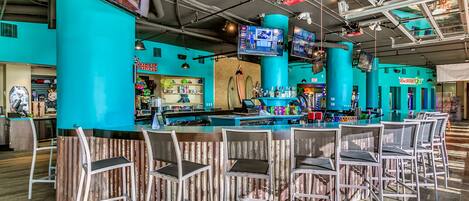 A bar area with teal pillars, multiple screens, and bar stools.