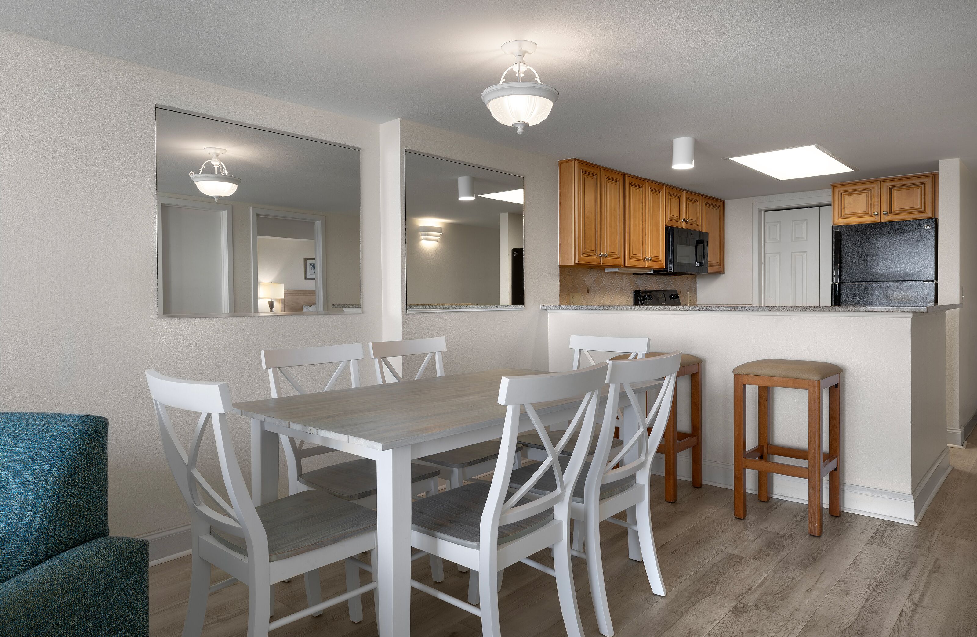 A modern kitchen with white cabinetry, a central island, and a dining area with white chairs and a wooden table.