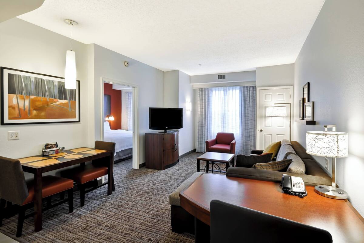A hotel room with a dining table, chairs, a TV, a sofa, a lamp, and a telephone.