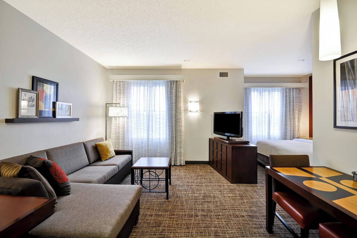 A hotel room with a sofa, a small table, a TV, and a bed.