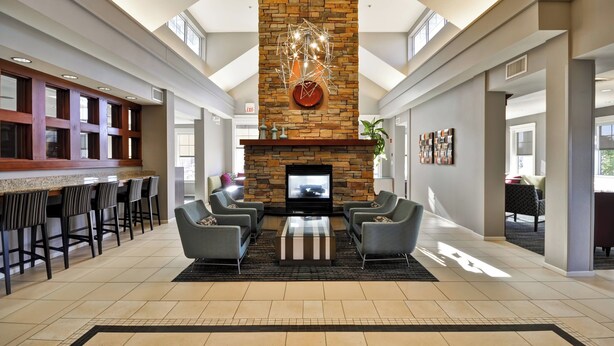 A spacious lobby with a stone fireplace, seating area, and a bar with high stools. - Residence Inn by Marriott O'Fallon (O'Fallon)