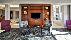A hotel lobby with a seating area featuring two armchairs, a round coffee table, and a flat-screen TV mounted on a wooden wall. - Residence Inn by Marriott O'Fallon (O'Fallon)