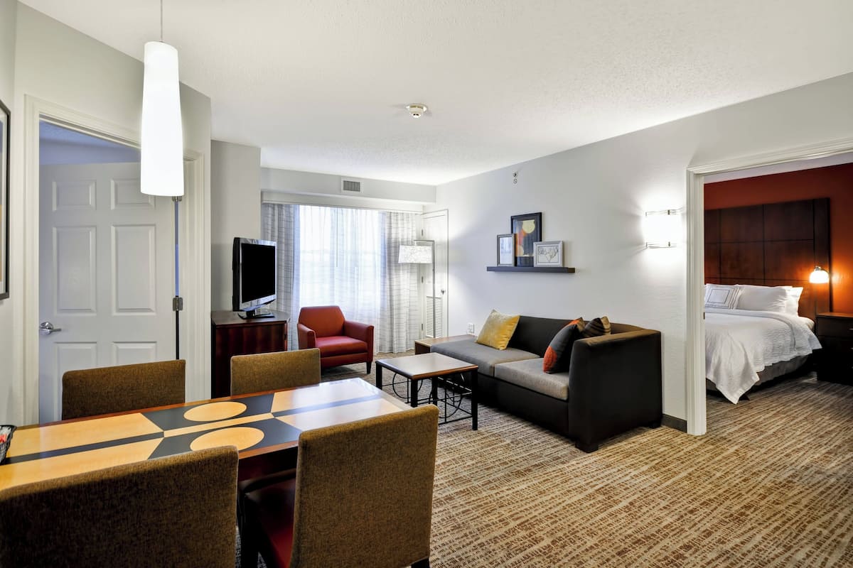 A hotel room with a dining area, a sofa, a TV, and a bed.