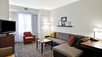Una sala de estar moderna con un televisor de pantalla plana, un sillón rojo, un sofá gris y una pequeña mesa.