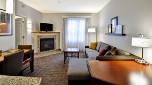 A modern living room with a fireplace, a flat-screen TV, a sofa, a coffee table, and a dining area. - Residence Inn by Marriott O'Fallon (O'Fallon)