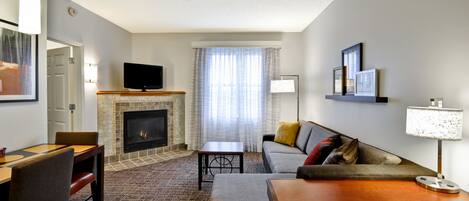 A modern living room with a fireplace, a flat-screen TV, a sofa, a coffee table, and a dining area.