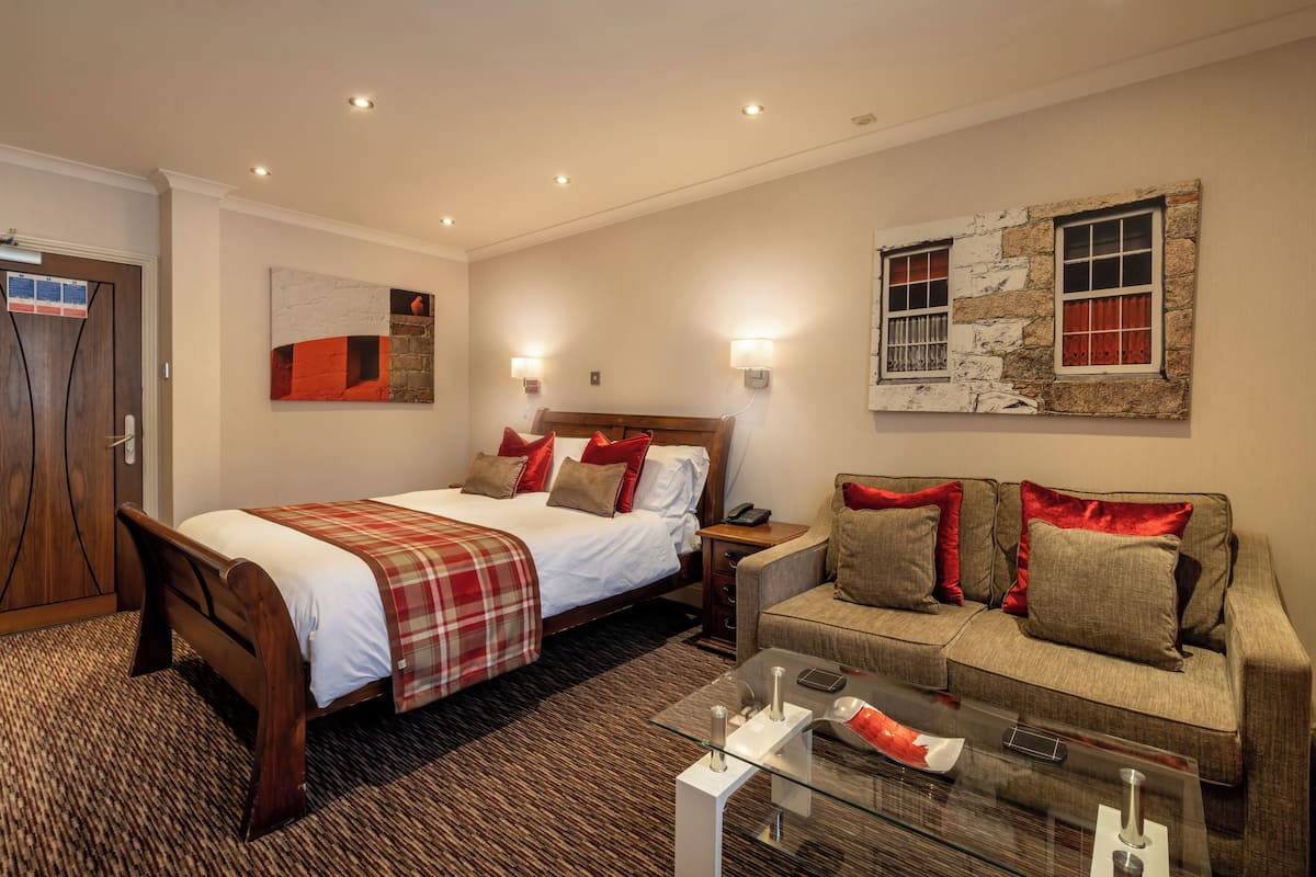 Una habitación de hotel con una cama, un sofá, una mesa de centro de vidrio y una obra de arte colgada en la pared.