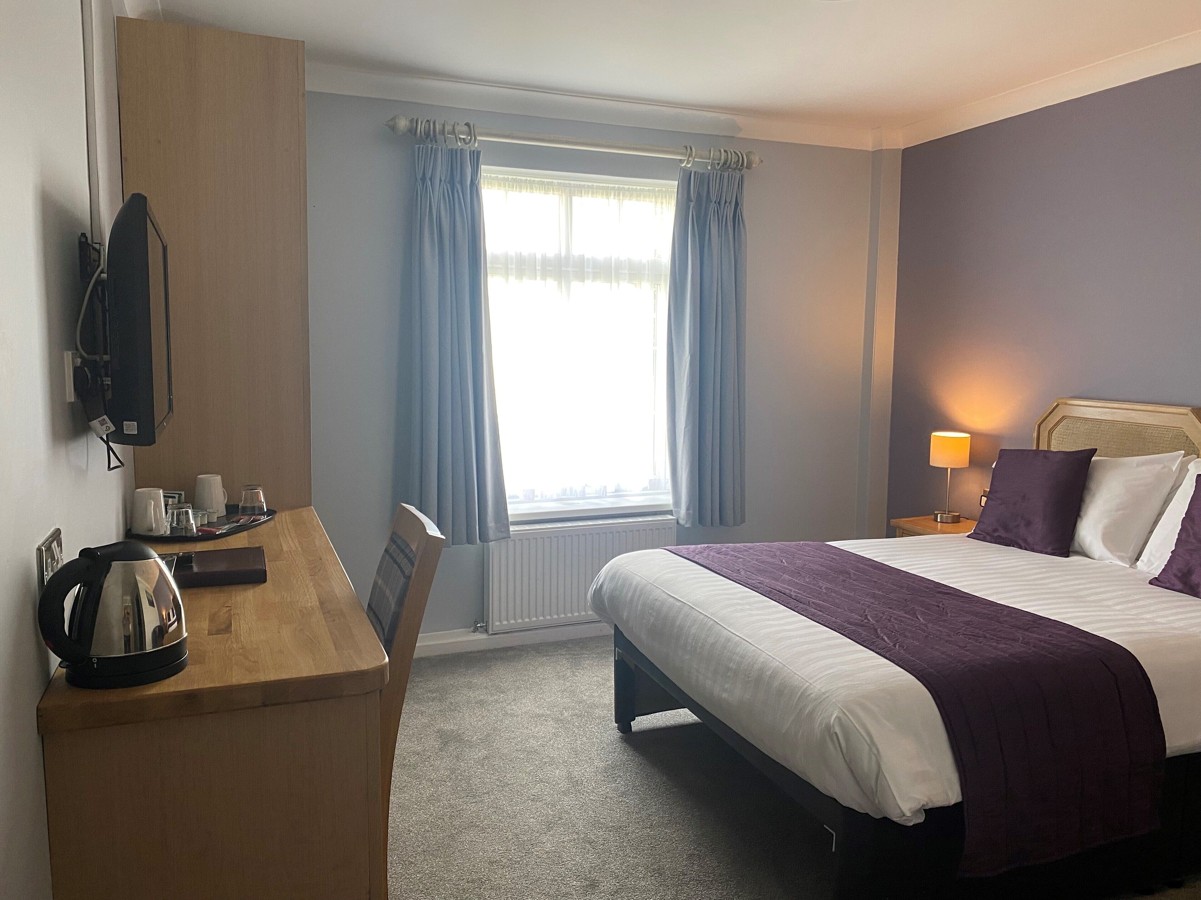 A hotel room with a bed, bedside table, TV, and a window with curtains.