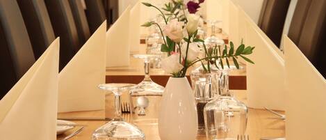 A conference table set with glassware, silverware, and a white vase with flowers.