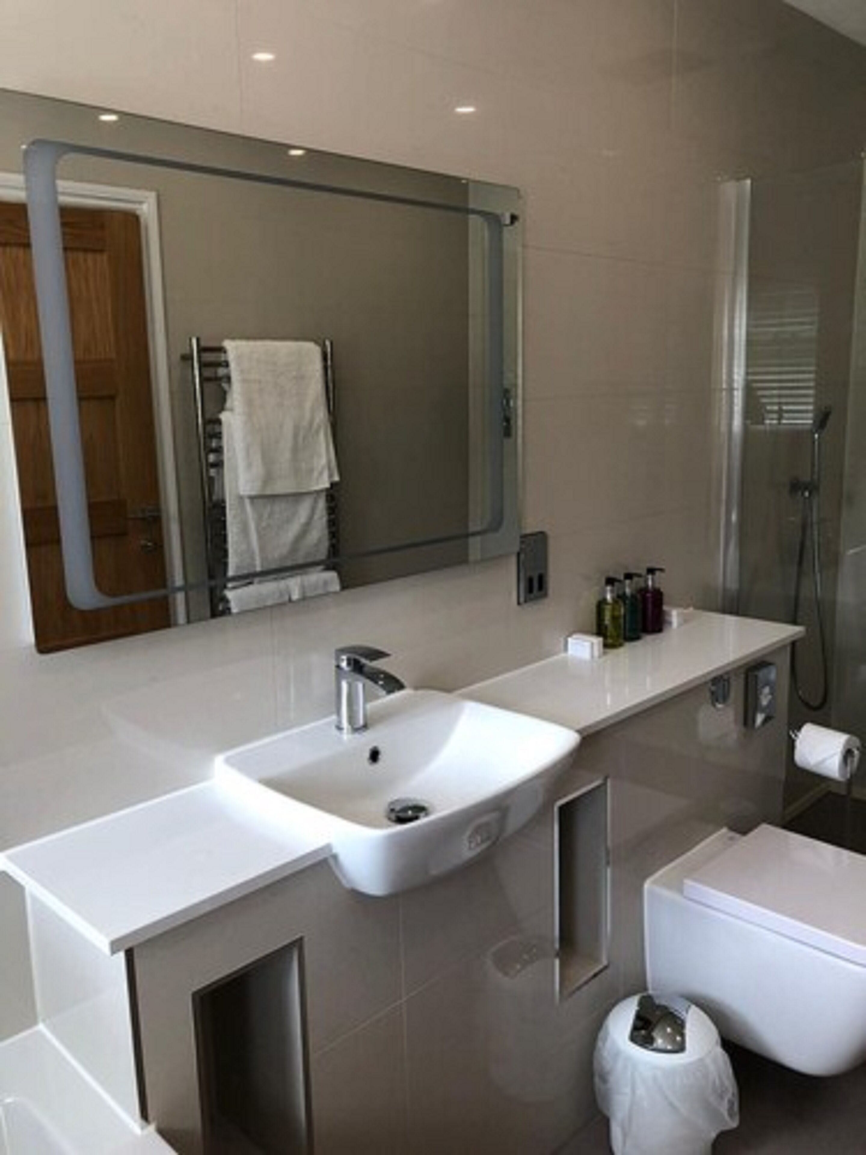 Un baño moderno con un espejo grande, un lavabo blanco, un inodoro y una ducha.