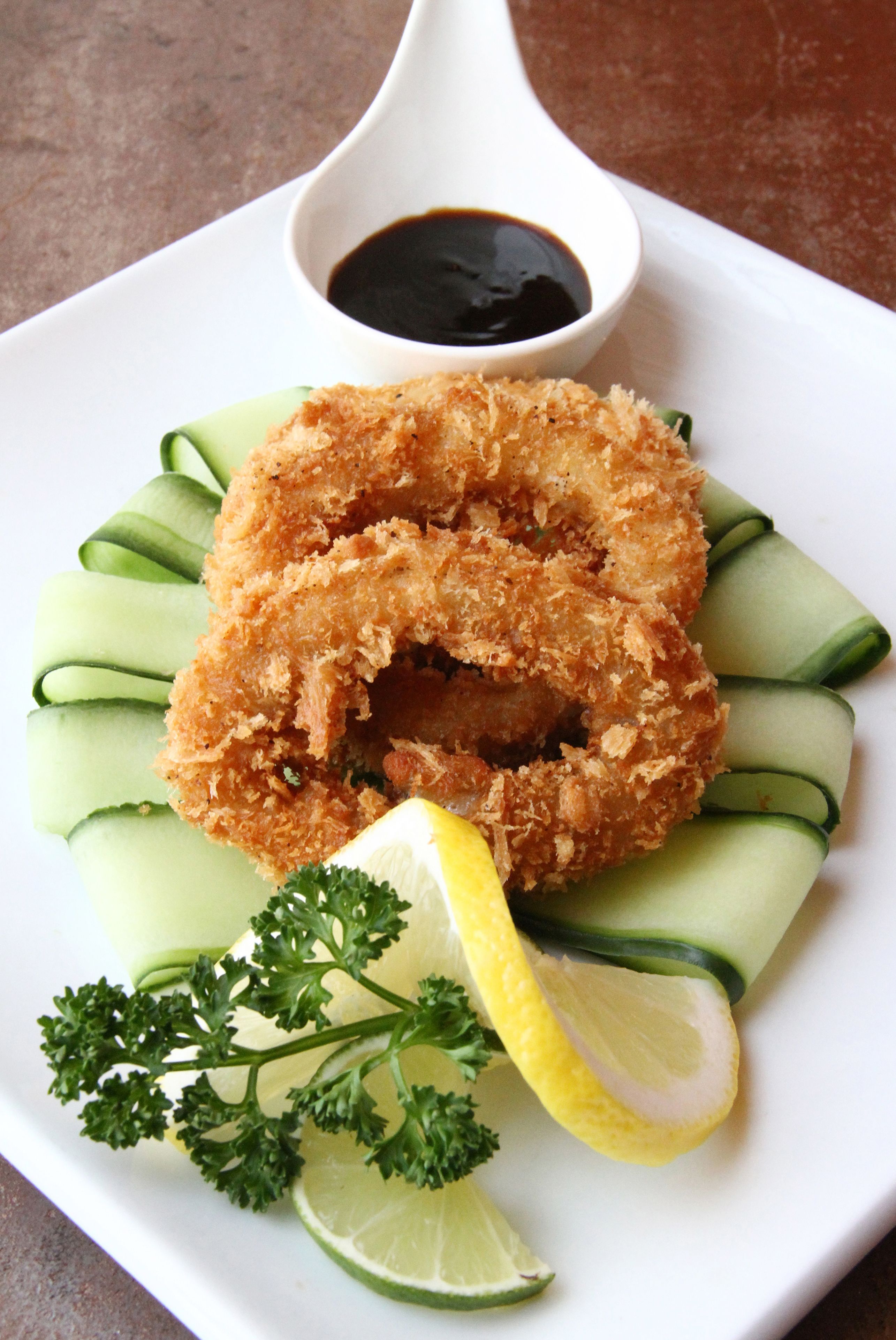 A plate with a fried item, cucumber slices, parsley, and a lemon wedge.