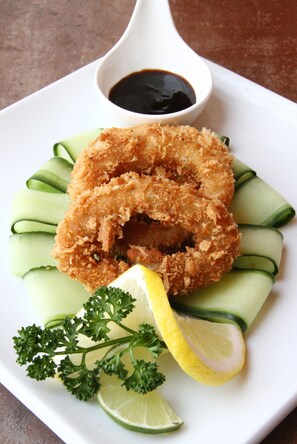 A plate with a fried item, cucumber slices, parsley, and a lemon wedge.