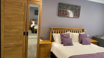 Un dormitorio con un armario de madera, una cama con ropa de cama blanca y morada, una mesita de noche y un cuadro en la pared.