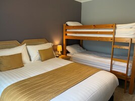 Habitación con literas, cabecera de madera, ropa de cama blanca y una lámpara de noche.