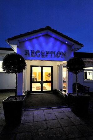 A reception area with a sign, glass doors, and two potted trees.