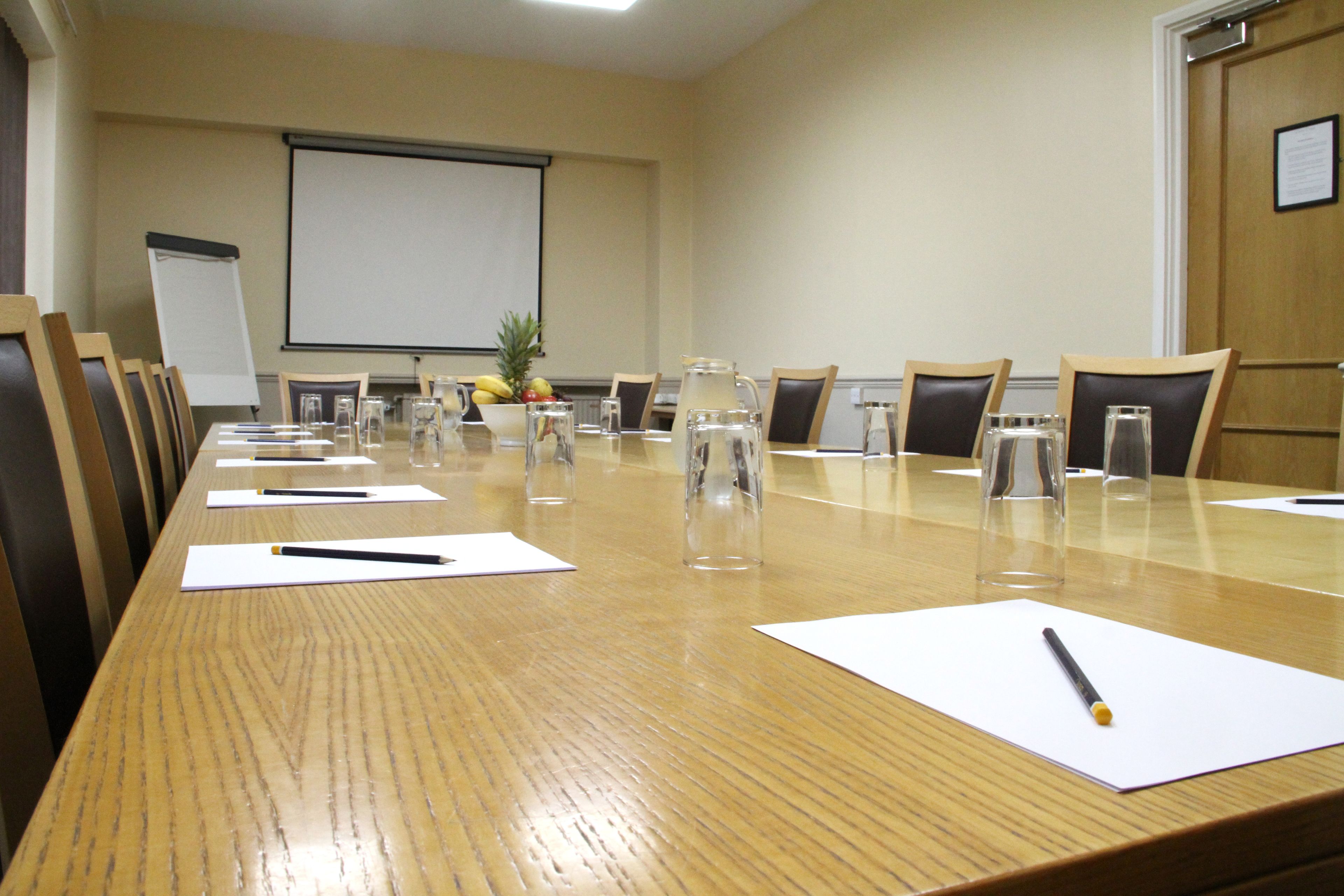 A conference room with a long table, chairs, a projector screen, and a whiteboard.