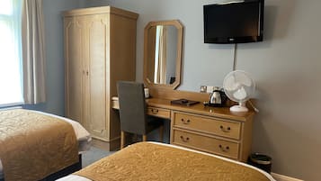 Habitación de hotel con dos camas, un armario, un escritorio con espejo, un televisor y un ventilador.