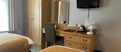 Habitación de hotel con dos camas, un armario, un escritorio con espejo, un televisor y un ventilador.