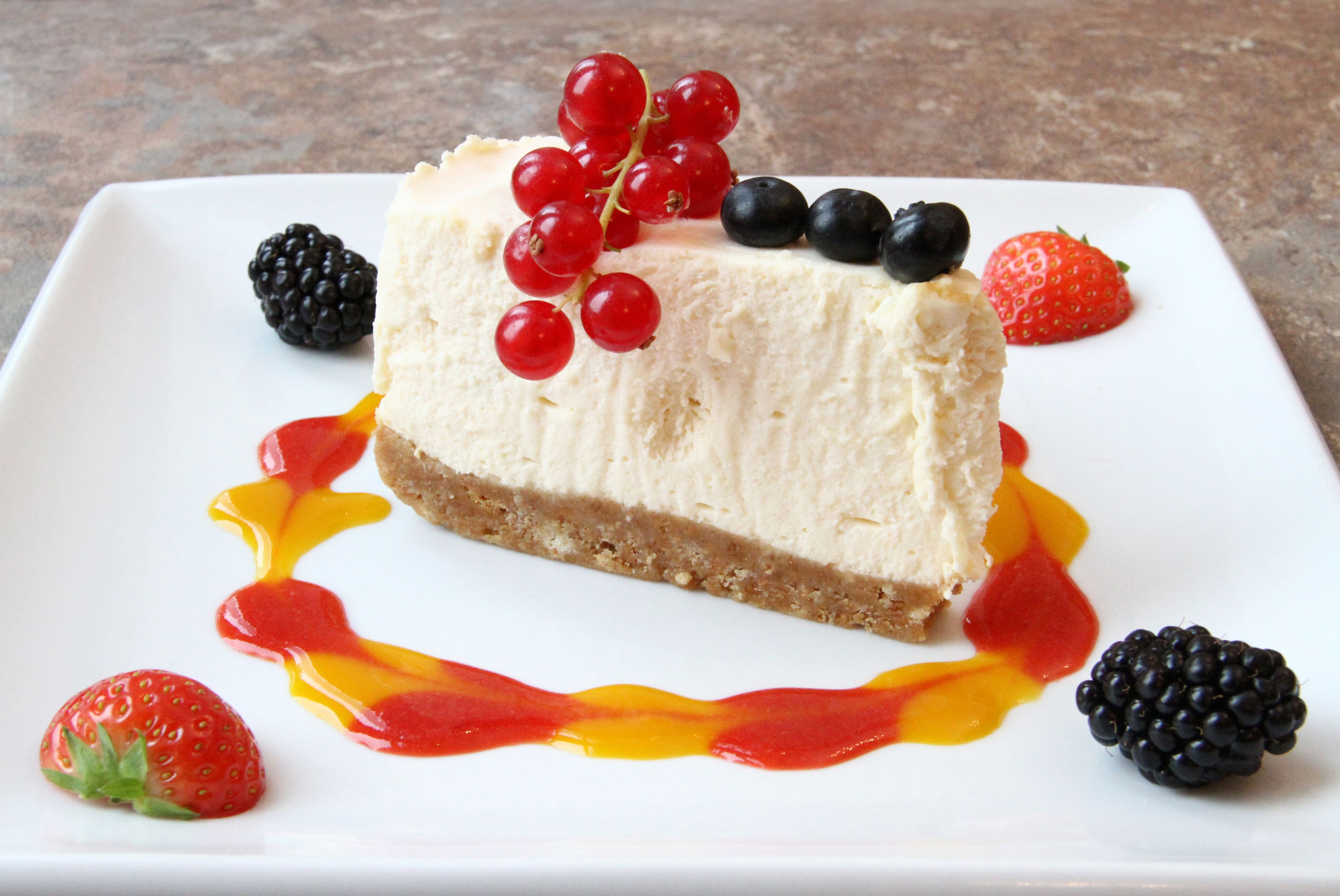 A slice of cheesecake with berries and a drizzle of sauce on a white plate.