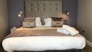Una cama bien hecha con un cabecero grande, una mesita de noche con lámpara y un reloj de pared.