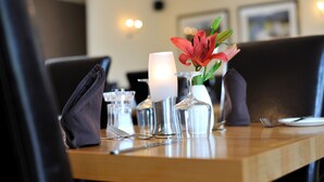 Una mesa de comedor dispuesta con una vela, un florero con una flor roja y cristalería transparente.