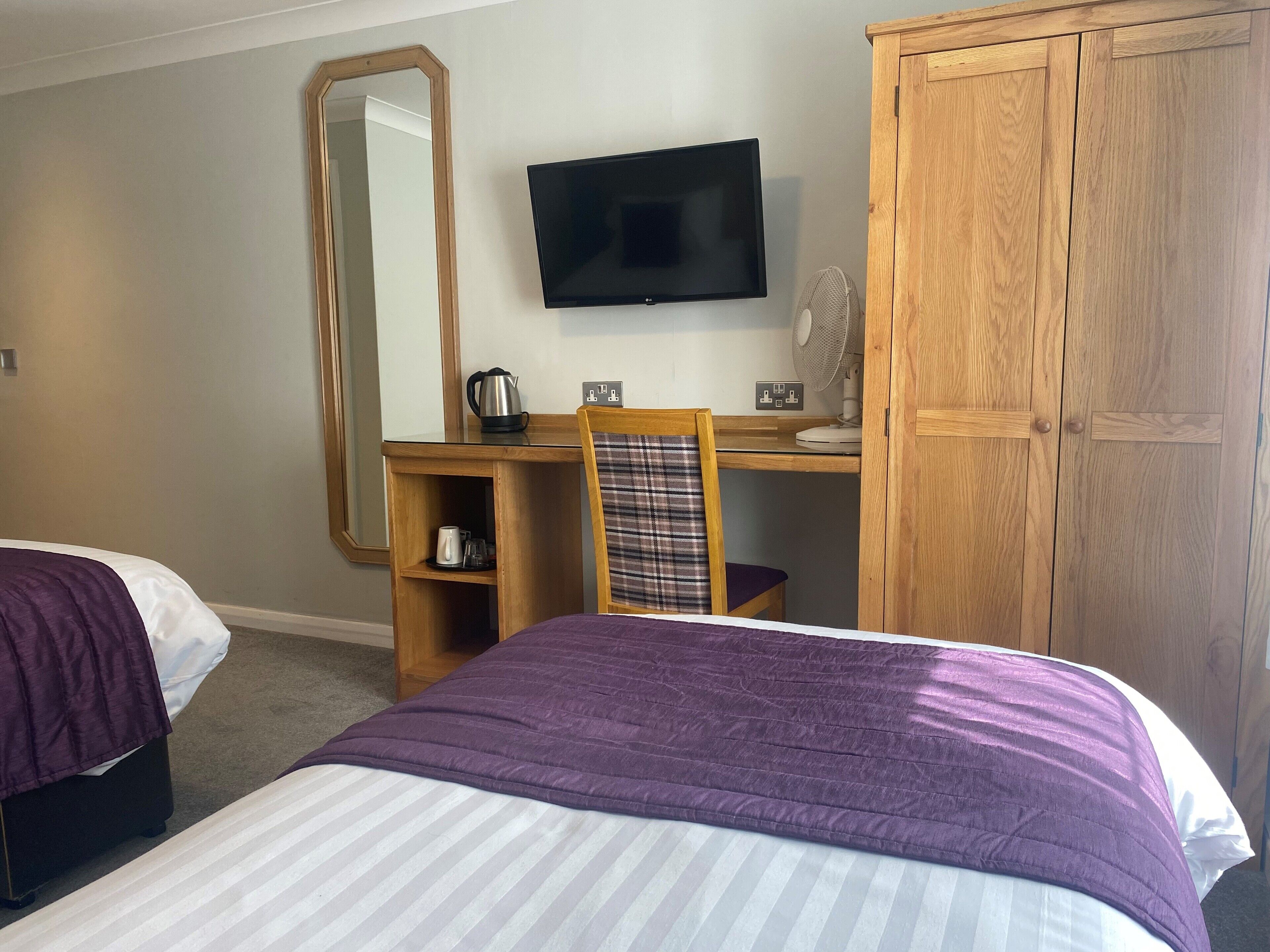 A hotel room with a bed, a desk with a chair, a television, a wardrobe, and a mirror.