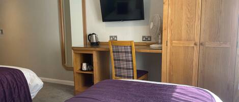 Habitación de hotel con cama, escritorio con silla, televisor, armario y espejo.