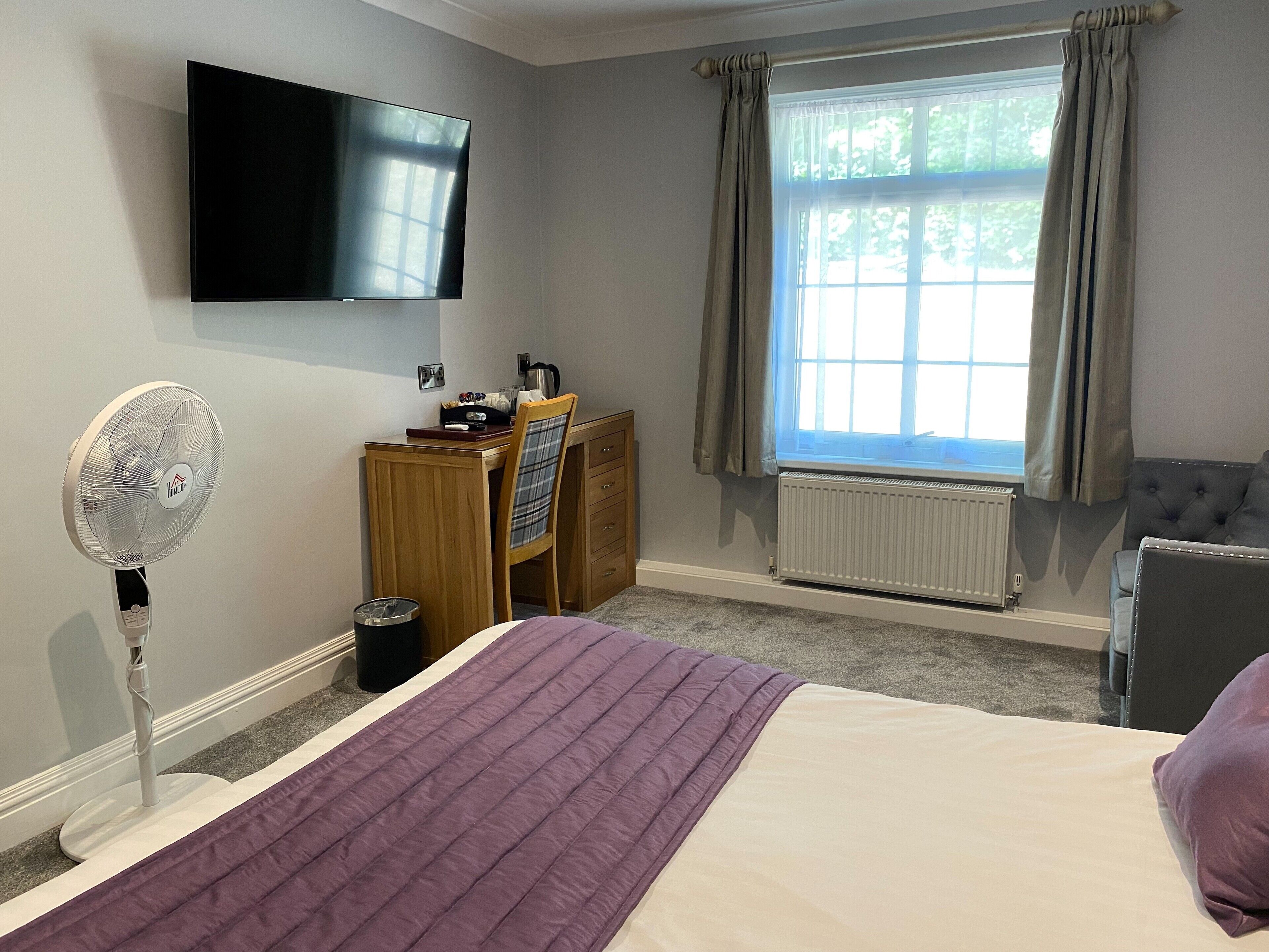 Een hotelkamer met een bed, een bureau, een stoel, een televisie en een raam met gordijnen.