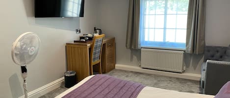 Een hotelkamer met een bed, een bureau, een stoel, een televisie en een raam met gordijnen.