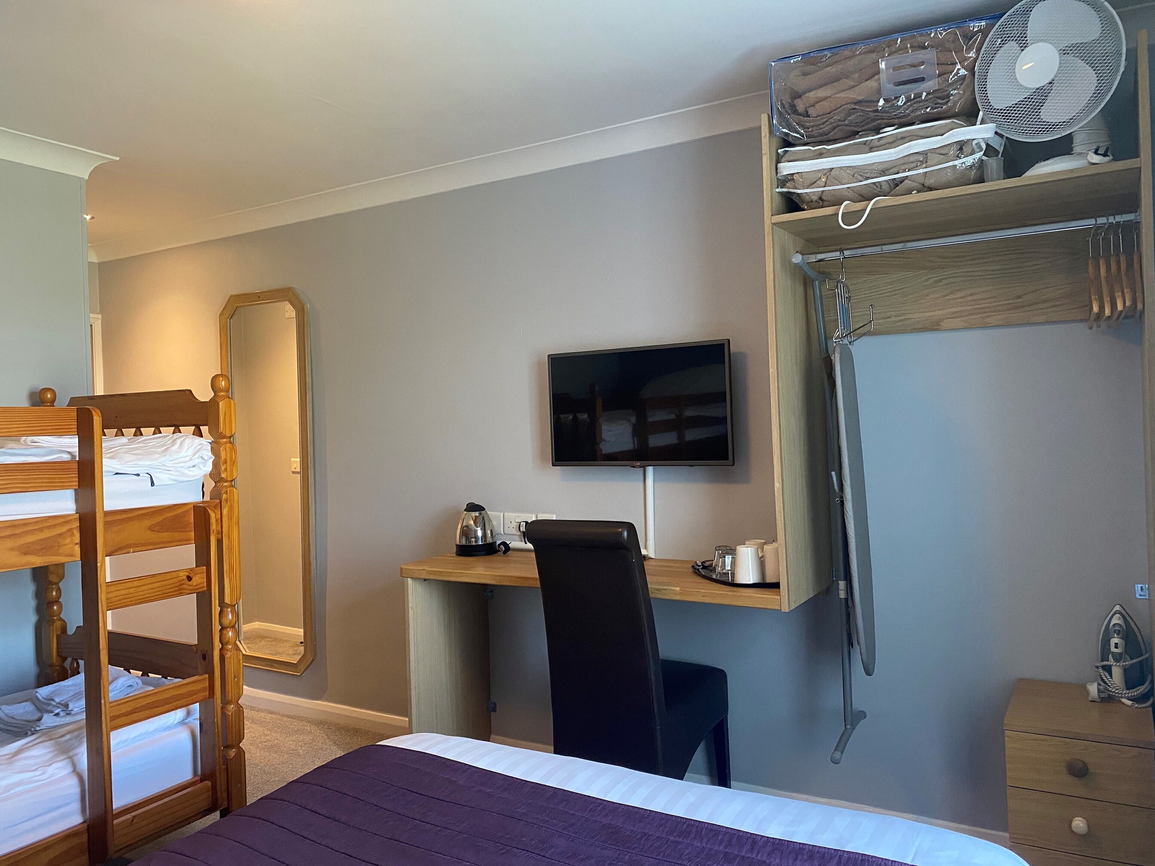 A bedroom with a bunk bed, a desk with a computer, a chair, a television, and a fan.