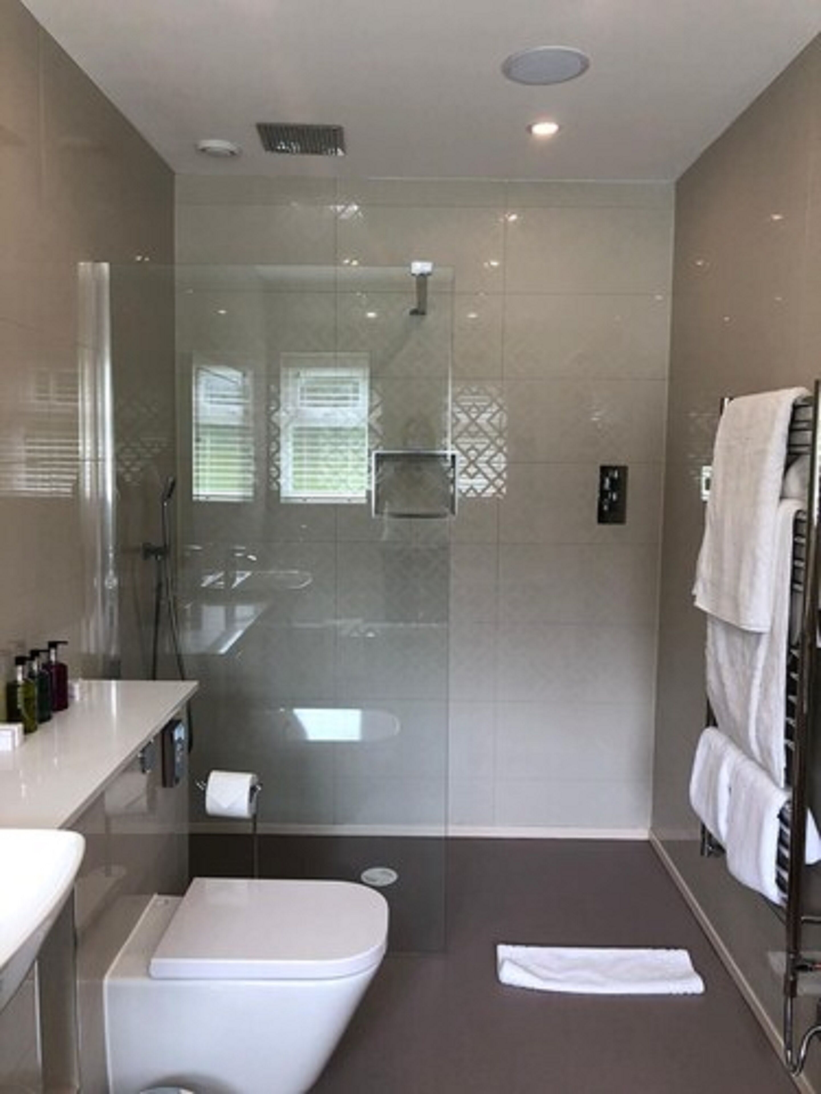 Un baño moderno con ducha de vidrio, inodoro blanco y un perchero con varias toallas.