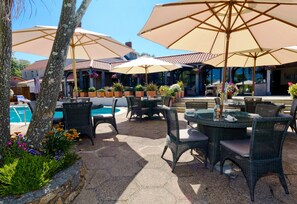 An outdoor patio area with wicker furniture, large umbrellas, and a pool.