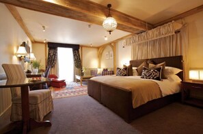 A bedroom with a large bed, a wooden ceiling, a chandelier, and a view of the outdoors.