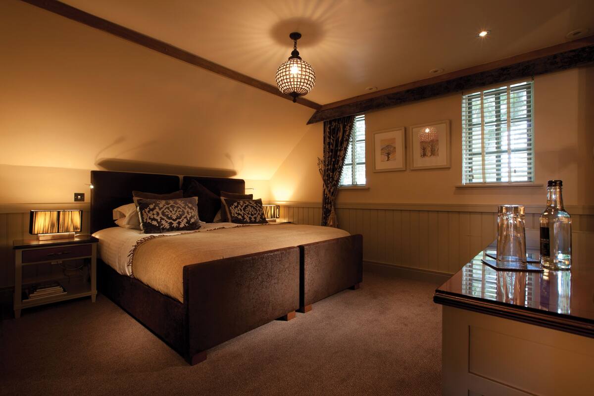 Um quarto com uma cama grande, mesas de cabeceira, luminária pendente, janela com persianas e mesa de cabeceira com abajur.