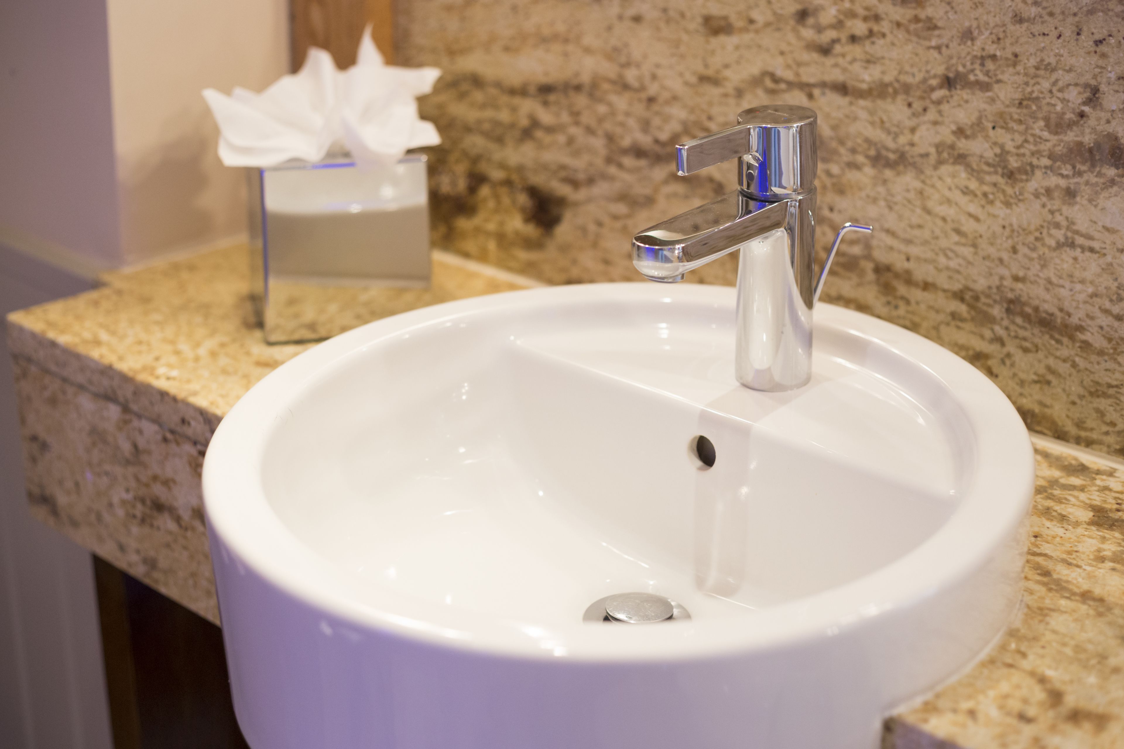 Un lavamanos blanco con grifo cromado en un baño con encimera de granito.