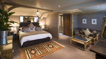A modern bedroom with a large bed, a sitting area with a sofa and coffee table, and a dining table.