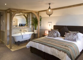 Un dormitorio con una cama grande, un arco de madera que da acceso a un baño, una araña y una mesita de noche con lámpara.