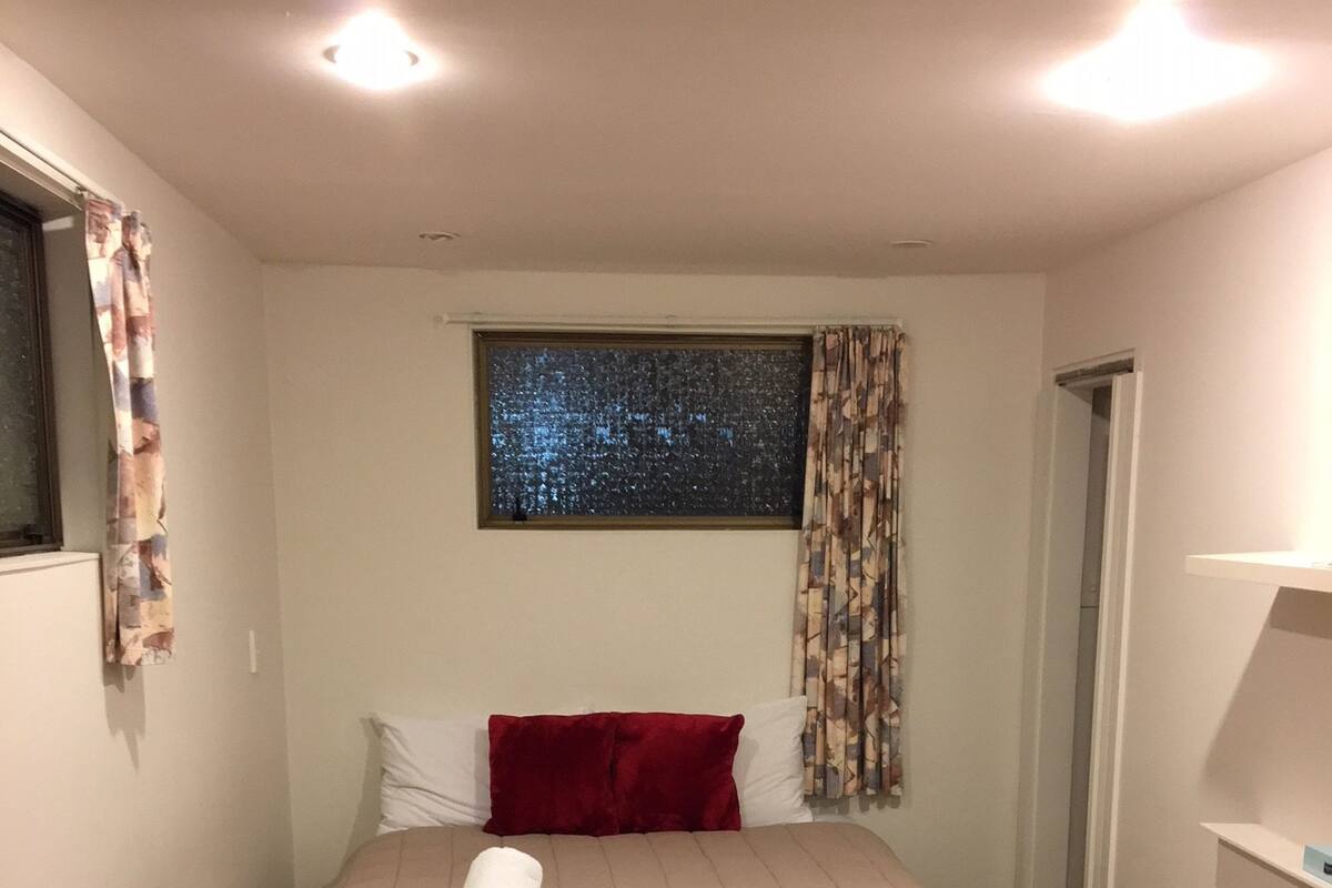 Une chambre d’hôtel avec un lit, une fenêtre donnant sur le ciel nocturne, un oreiller rouge et une chaise bleue.