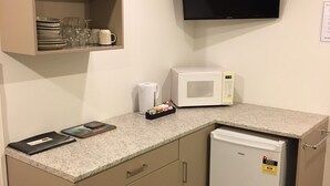 Een kleine keuken met een magnetron, een kleine koelkast en een kast met servies en glazen.