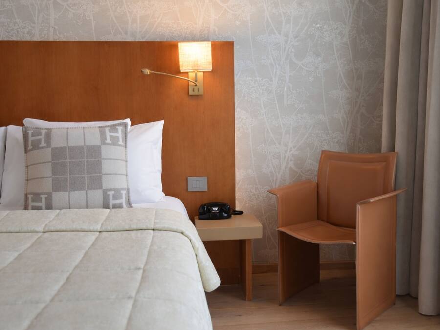 A hotel room with a bed, a nightstand with a lamp, a chair, and a wall with a floral pattern.