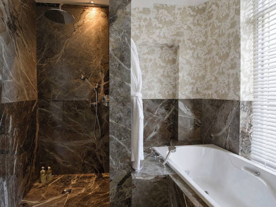 A bathroom with a shower, a bathtub, and marble walls.