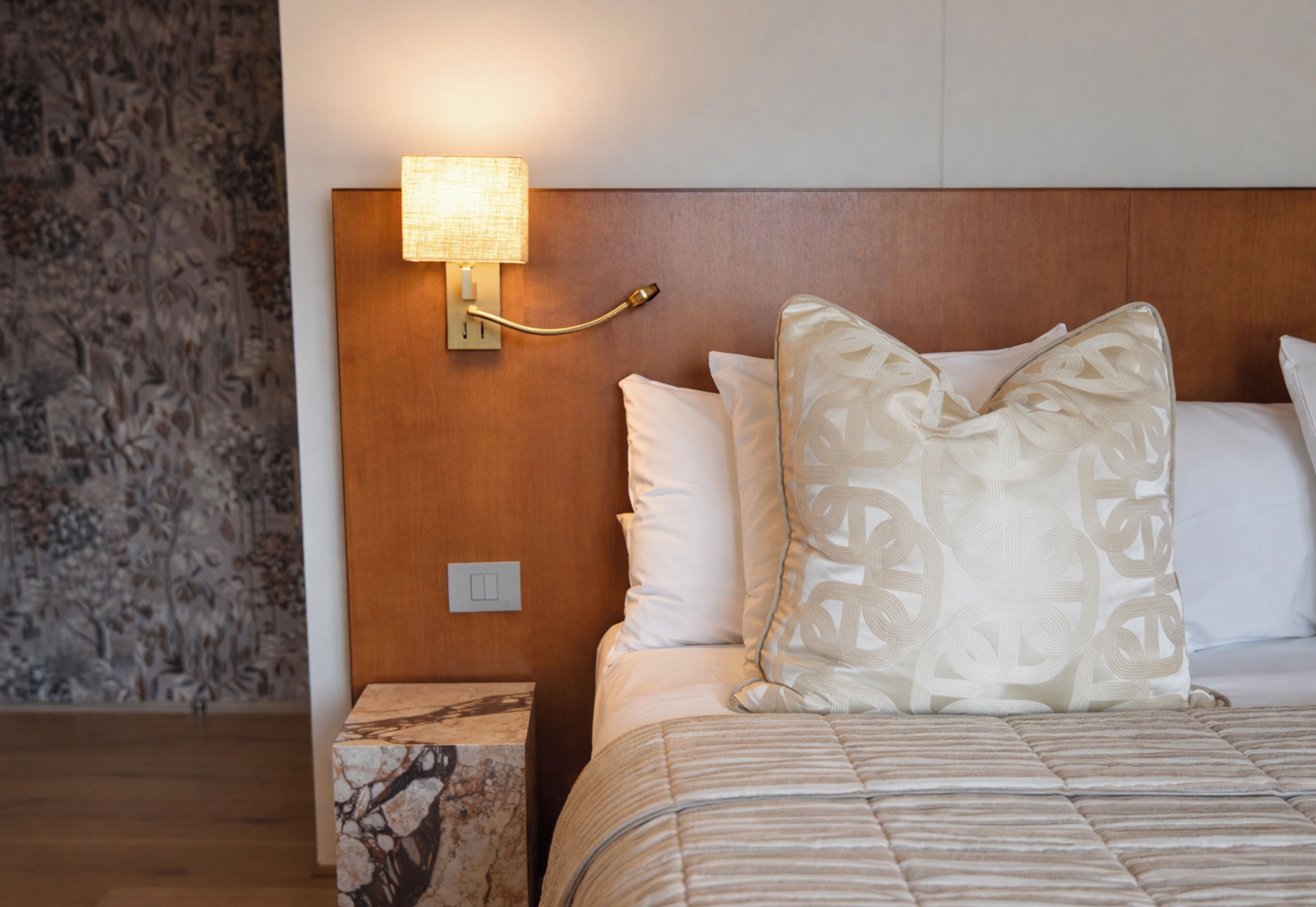 Una habitación de hotel con una cama, una mesita de noche, una lámpara de pared y una pared con diseño.