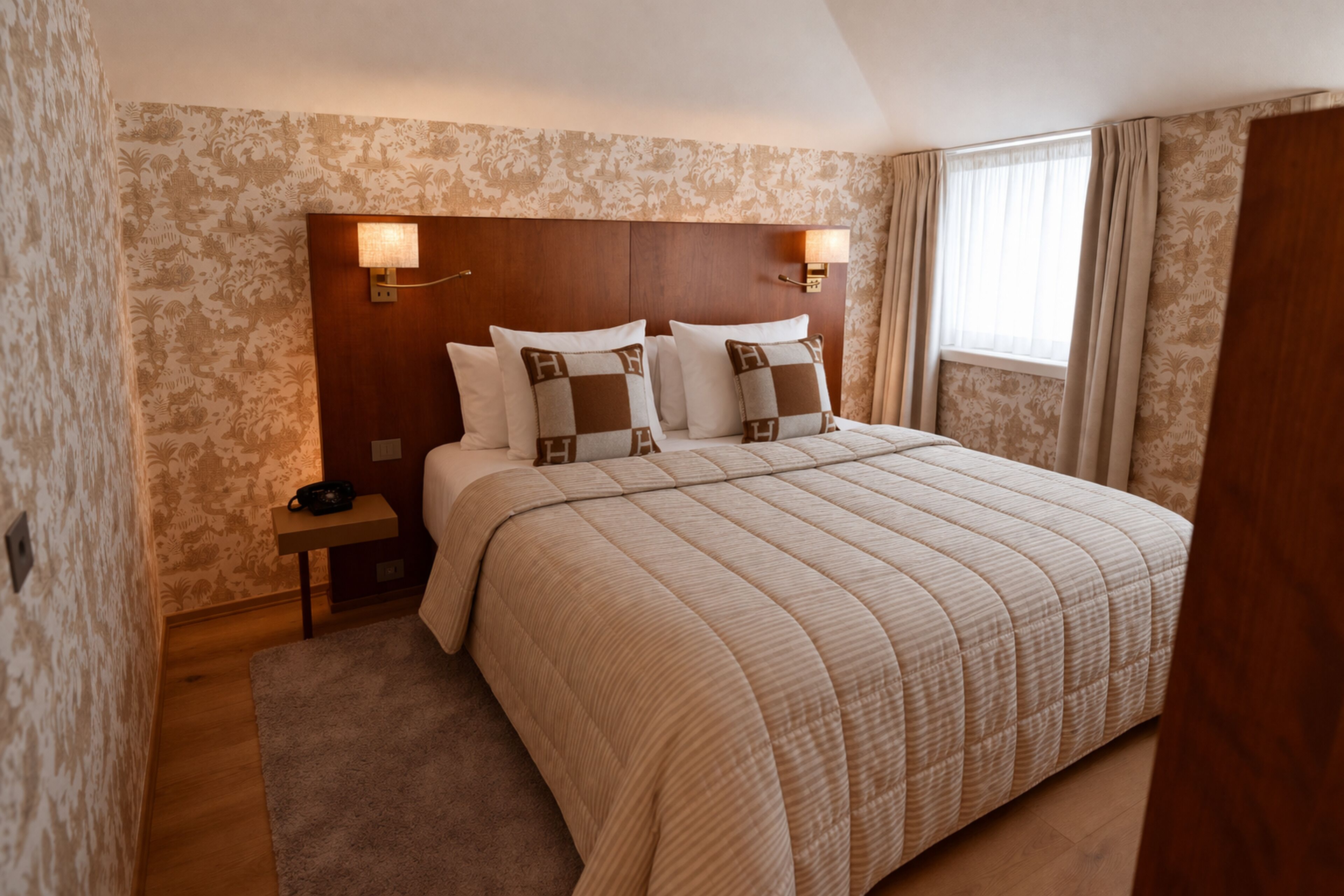 A hotel room with a large bed, a nightstand, a lamp, and a window with curtains.