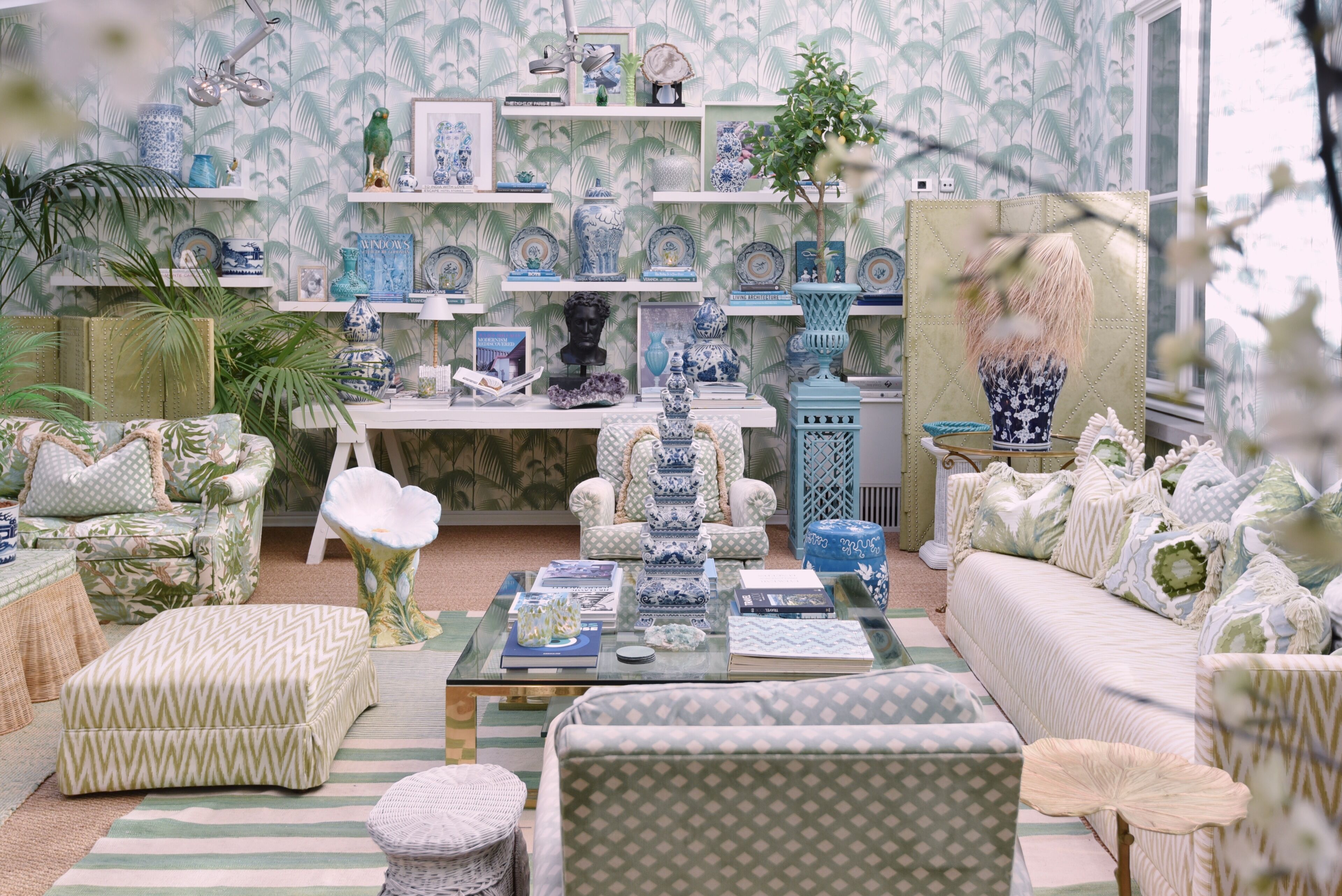 A room with a patterned wallpaper, a sofa, a coffee table, and a bookshelf with various decorative items.