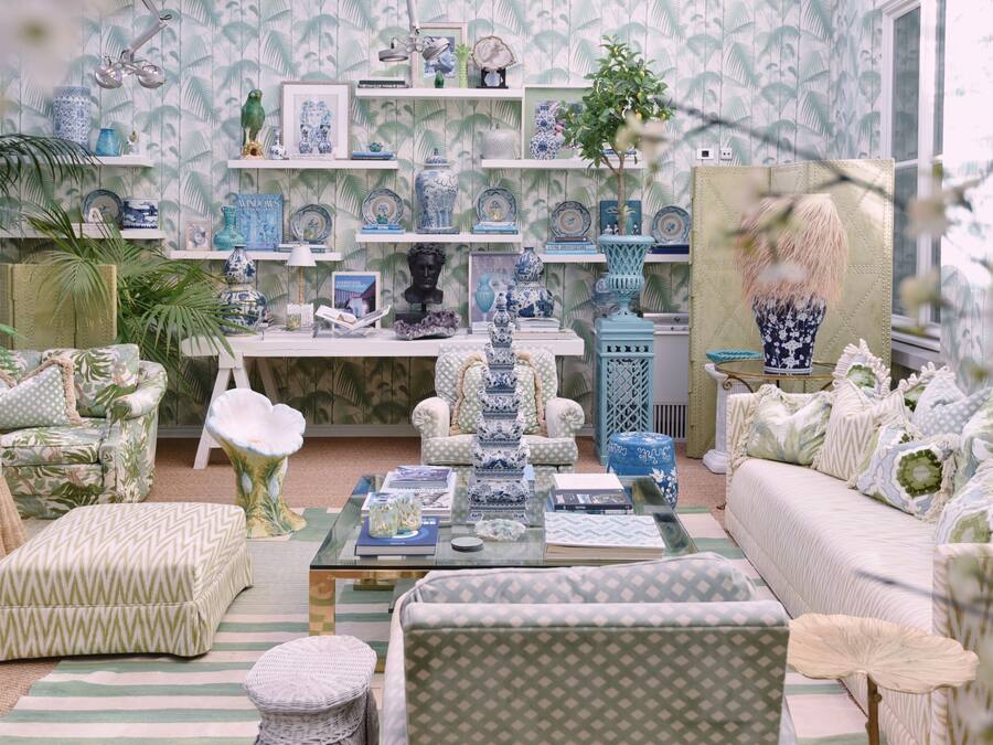A room with a patterned wallpaper, a sofa, a coffee table, and a bookshelf with various decorative items.