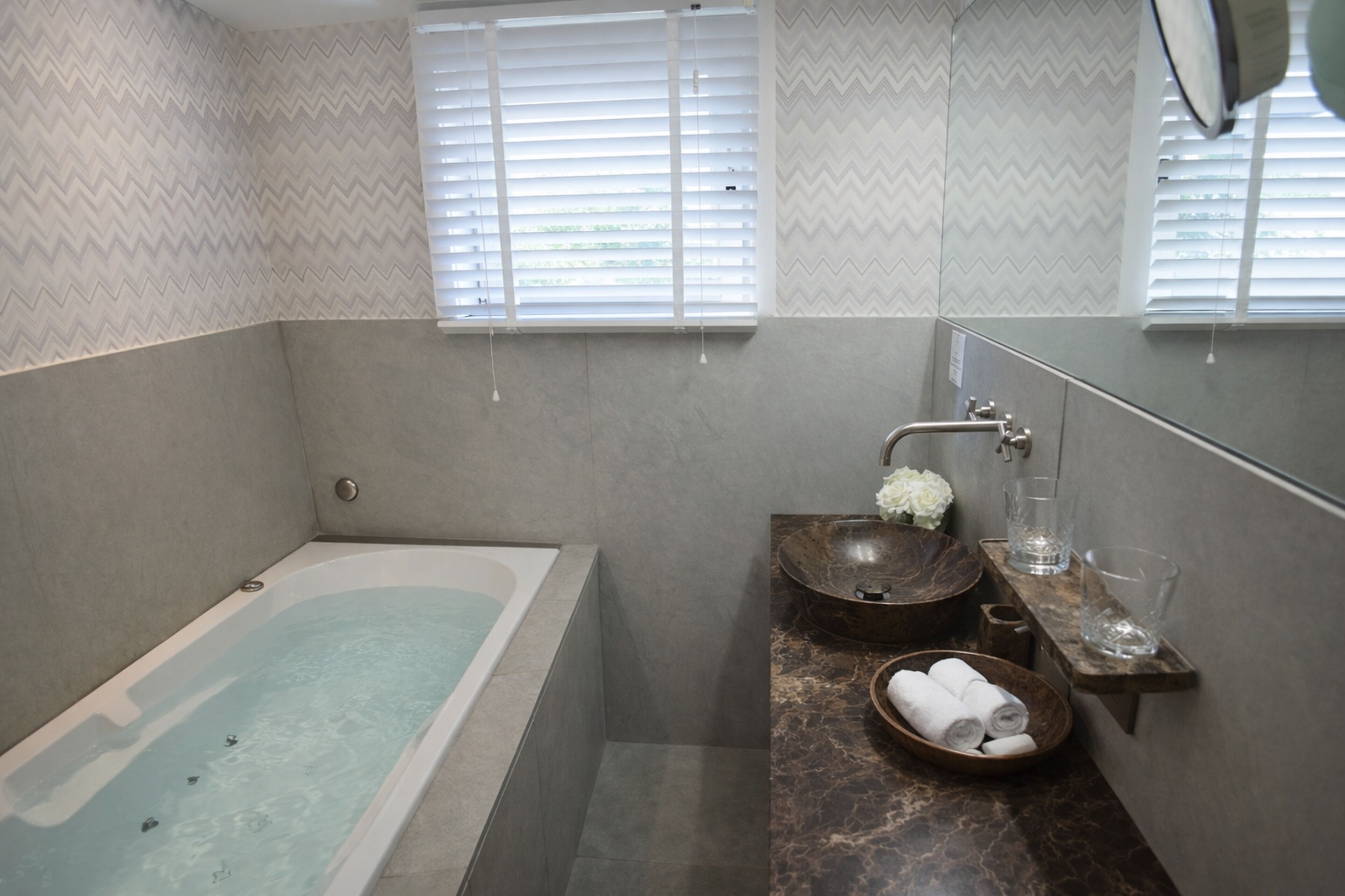 A modern bathroom with a bathtub, a wooden bowl sink, and a marble countertop.