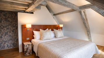 A bedroom with a sloped ceiling, wooden beams, a bed with a headboard, and two wall-mounted lamps.