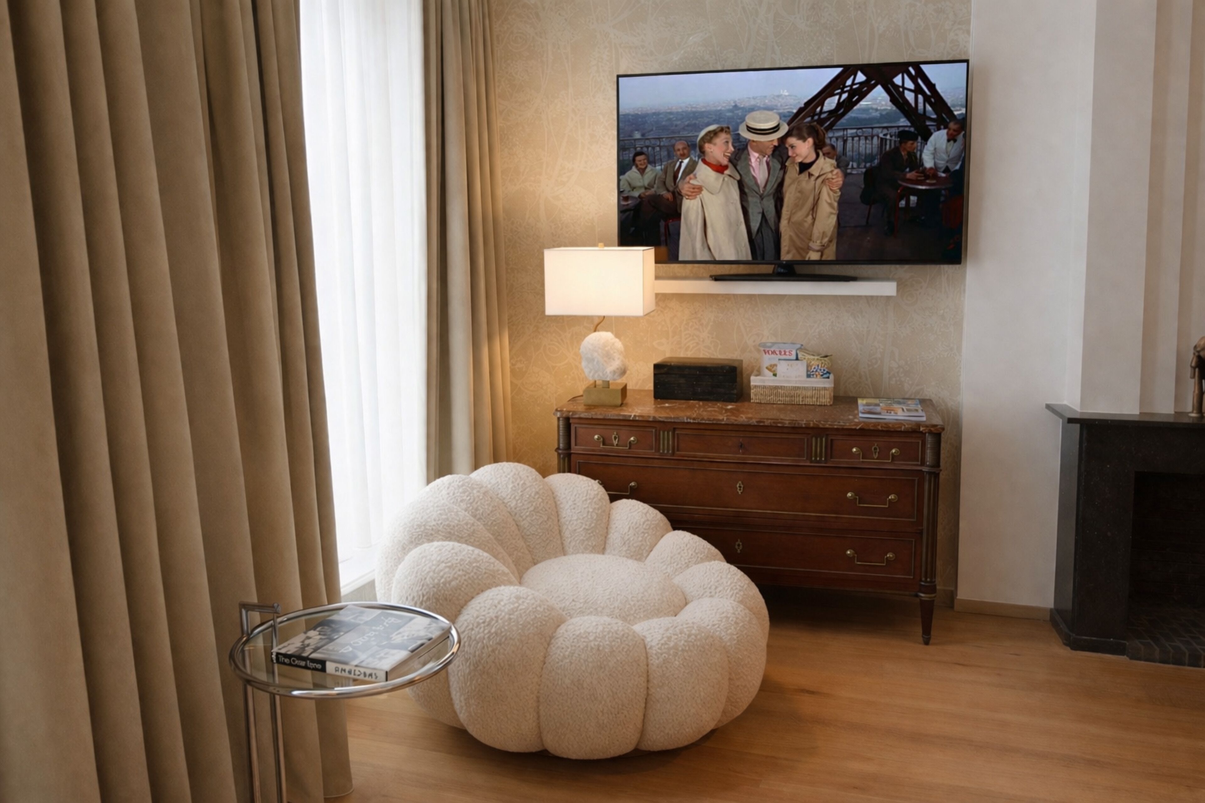A living room with a television mounted on the wall, a round ottoman, a wooden dresser, and a fireplace.