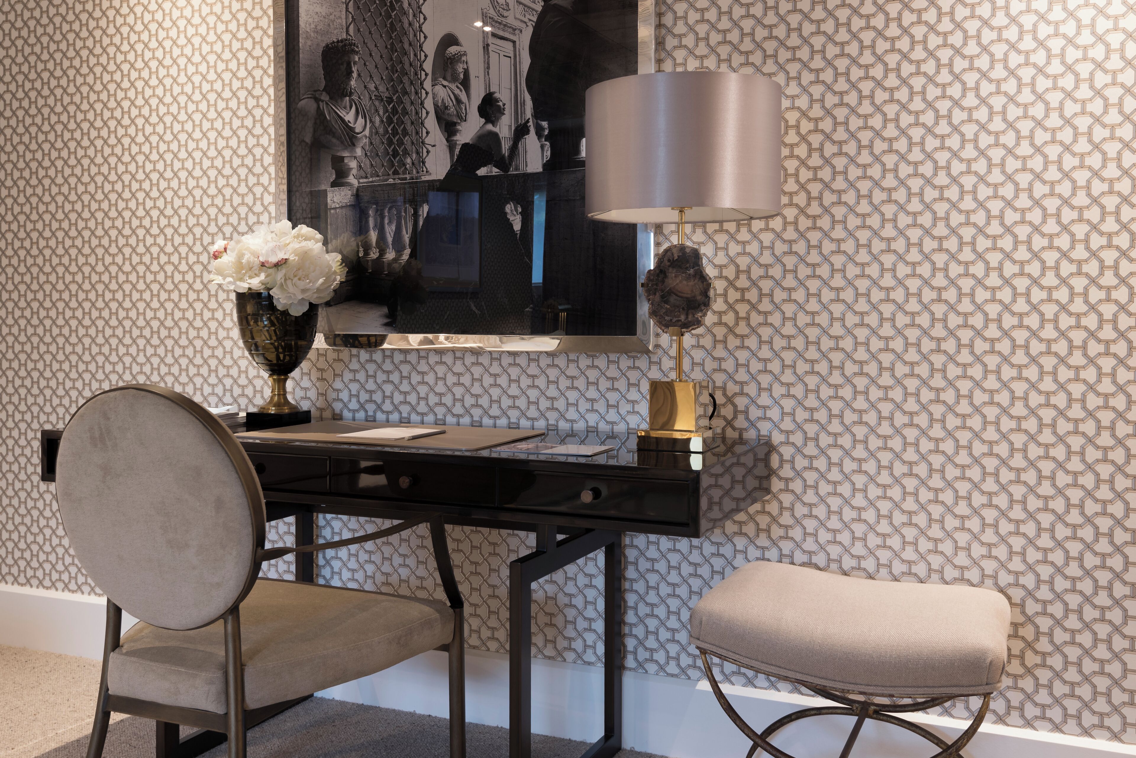 A desk with a chair, a lamp, and a vase with flowers.